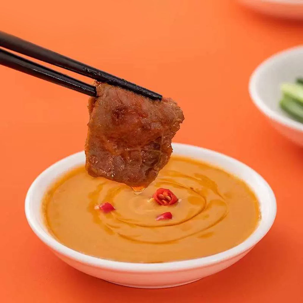 Chopsticks dipping grilled meat into HAIDILAO Spicy Hot Pot Dipping Sauce with chili