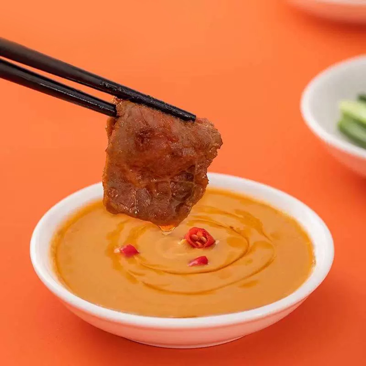 Chopsticks dipping grilled meat into HAIDILAO Spicy Hot Pot Dipping Sauce with chili