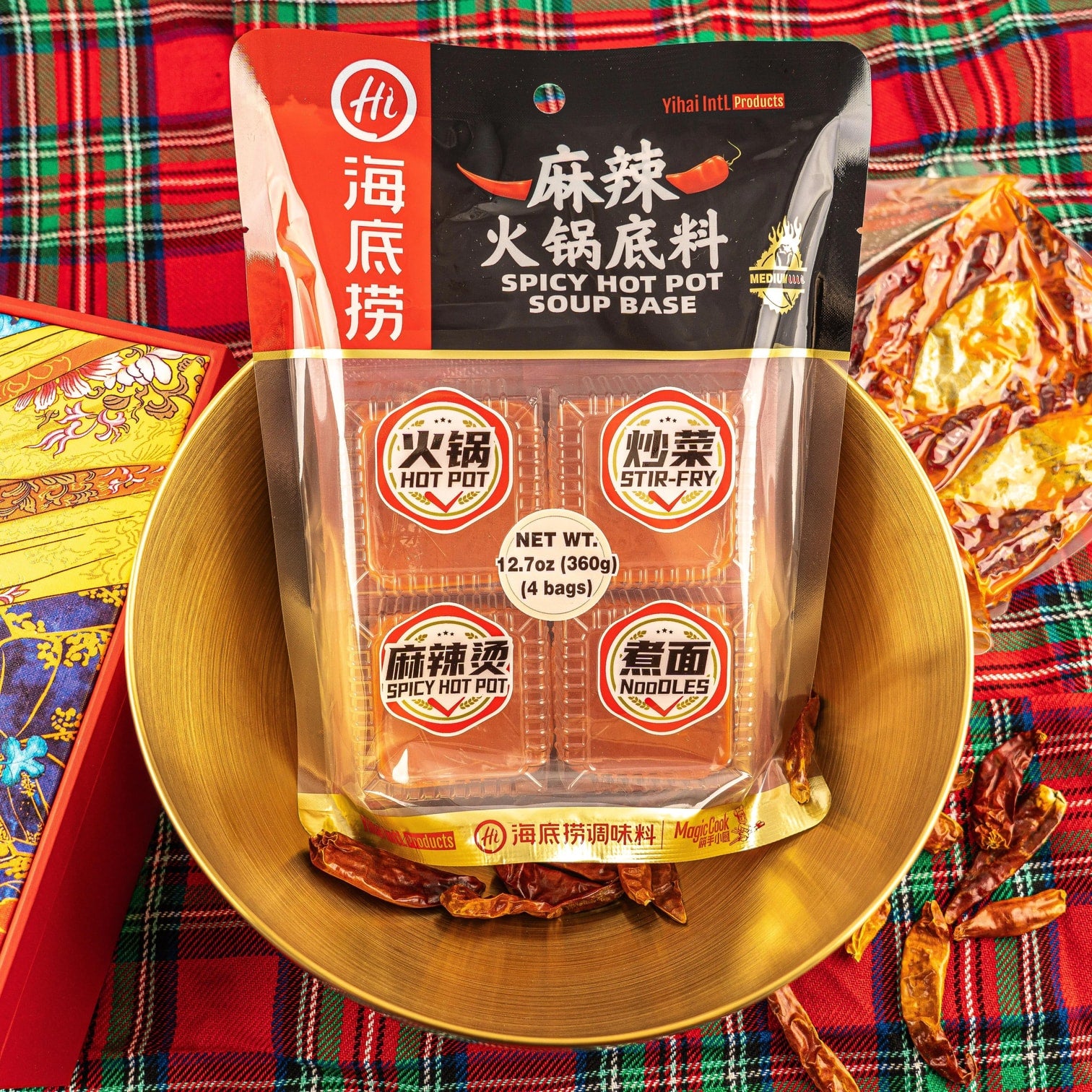 HAIDILAO Spicy Hot Pot Soup Base package displayed in a gold bowl with dried chili peppers on plaid fabric