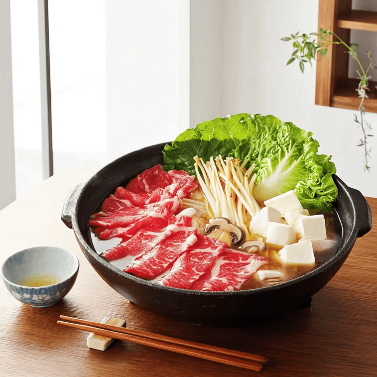 Cast iron sukiyaki pot with thin-sliced marbled beef, napa cabbage, enoki and shiitake mushrooms, and tofu, served with a small bowl of beaten egg and chopsticks