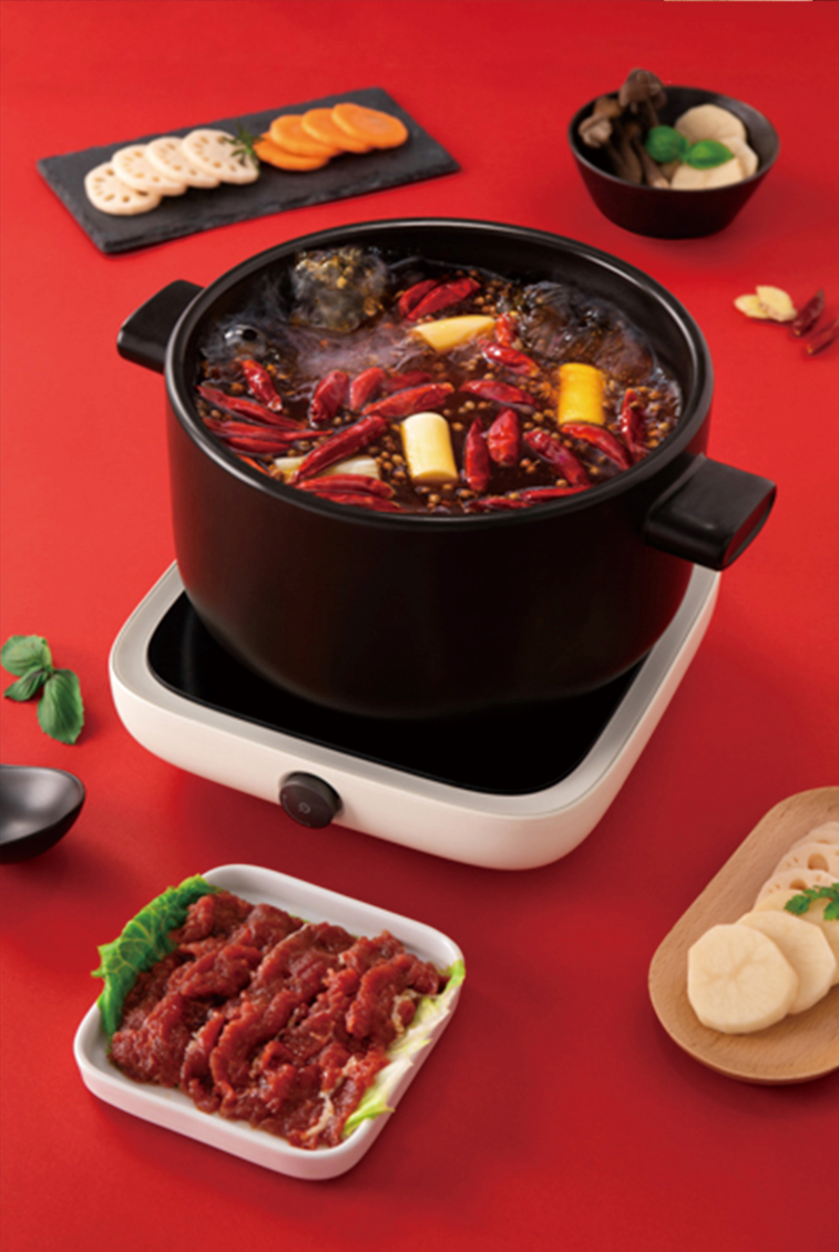 Bubbling pot of HAIDILAO Hot & Spicy Hot Pot with dried chilies, sliced meat, and hot pot ingredients on a portable stove