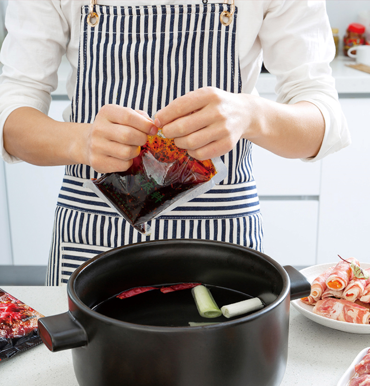 Tearing open a HAIDILAO Hot & Spicy Hot Pot Soup Base packet to add to a pot with scallions and dried chilies