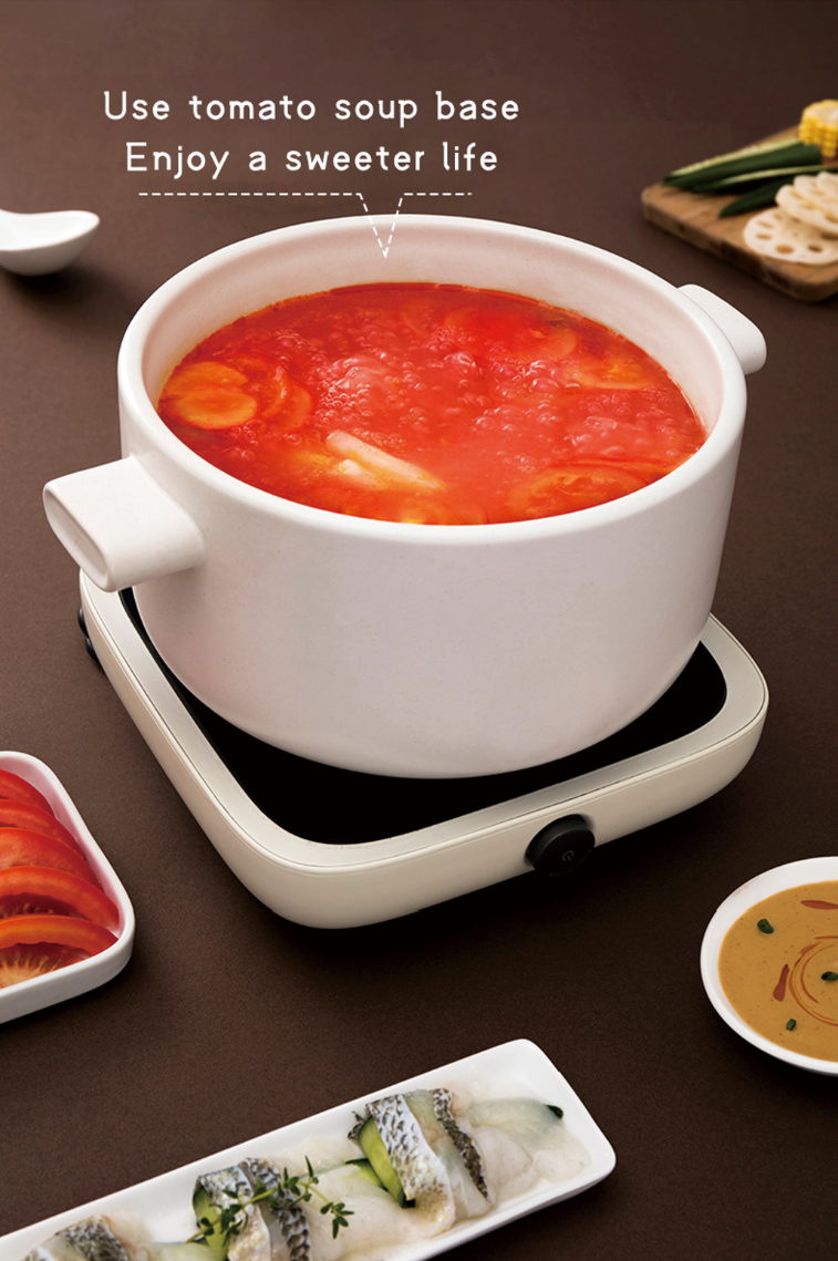 Bowl of HAIDILAO Tomato Soup Base hot pot broth simmering on a portable stove, served with hot pot ingredients